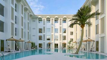 A pool area with lounge chairs and umbrellas, surrounded by a multi-story building with balconies.