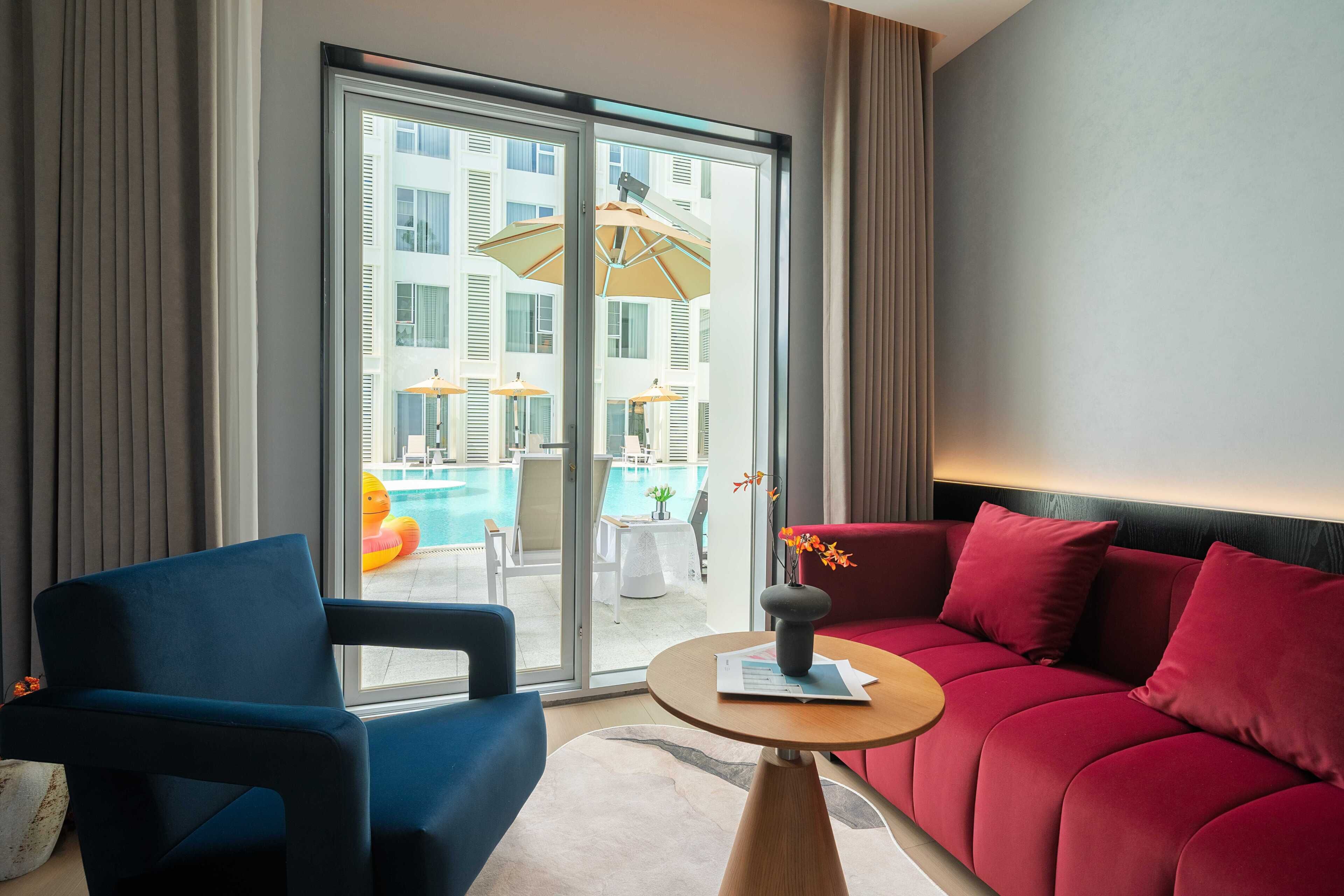 A modern hotel room with a blue armchair, a red sofa, and a small table with a vase.