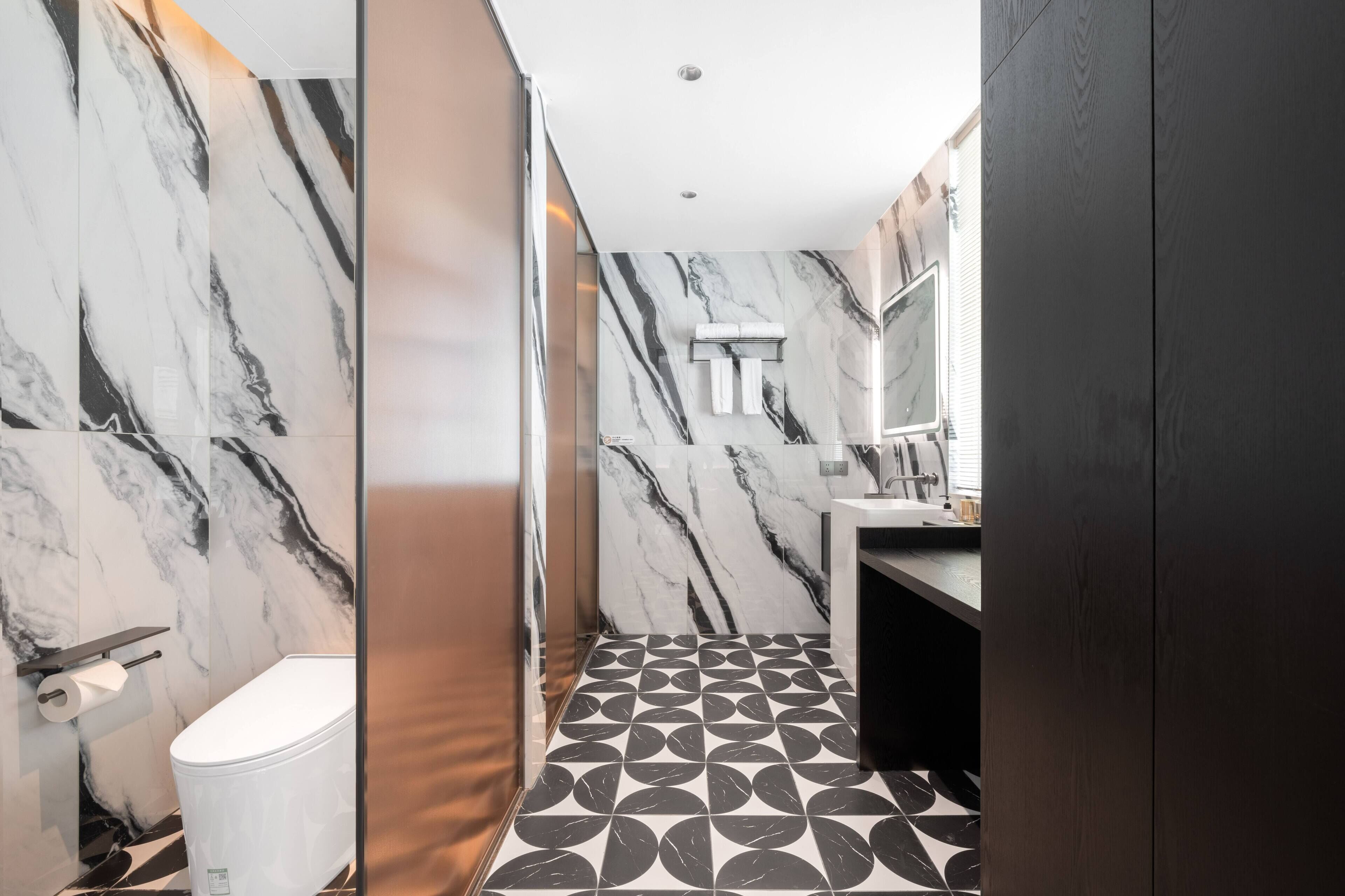 A modern bathroom with a marble wall, a toilet, a sink, and a mirror.
