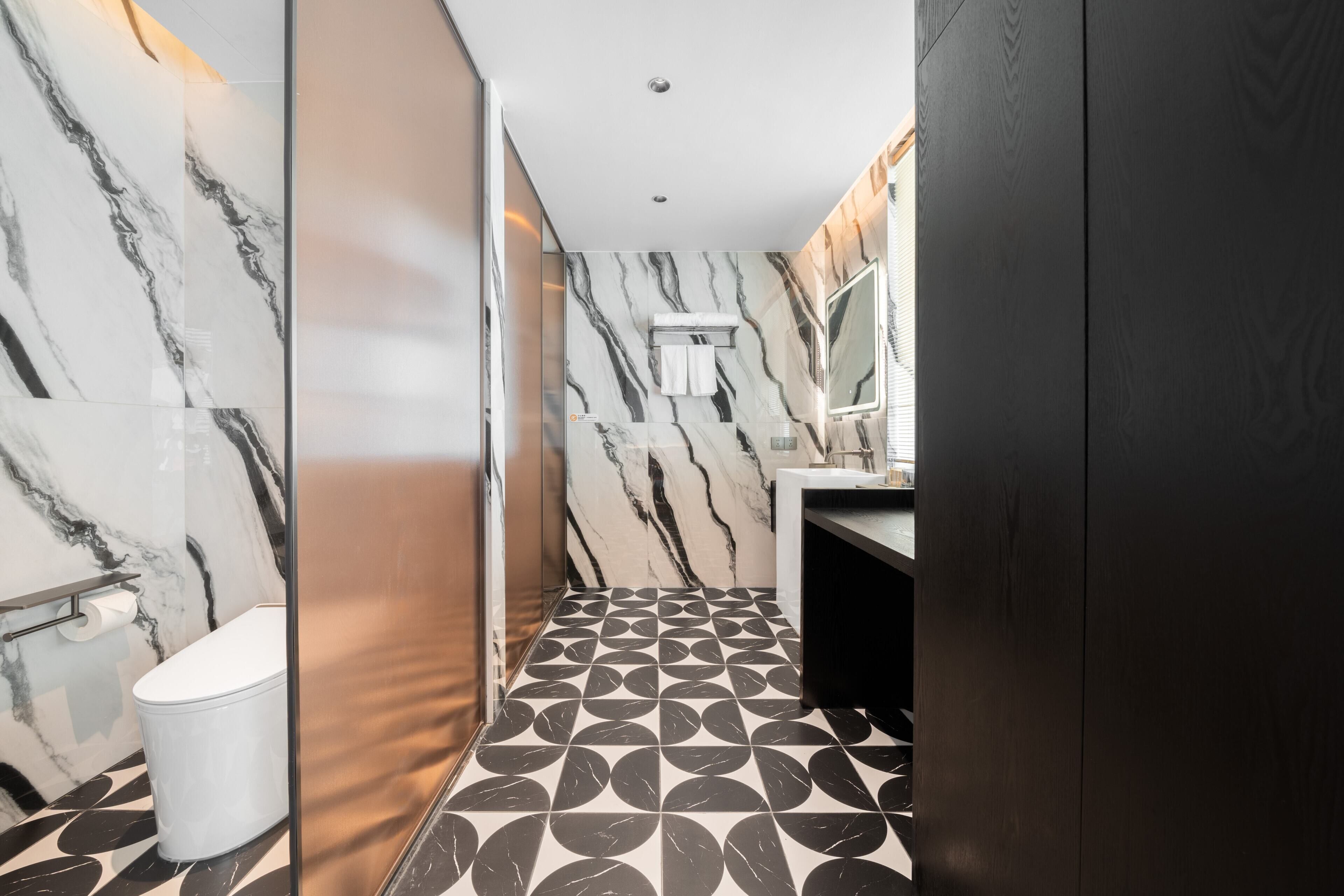 A modern bathroom with a marble wall, a toilet, a sink, and a patterned floor.