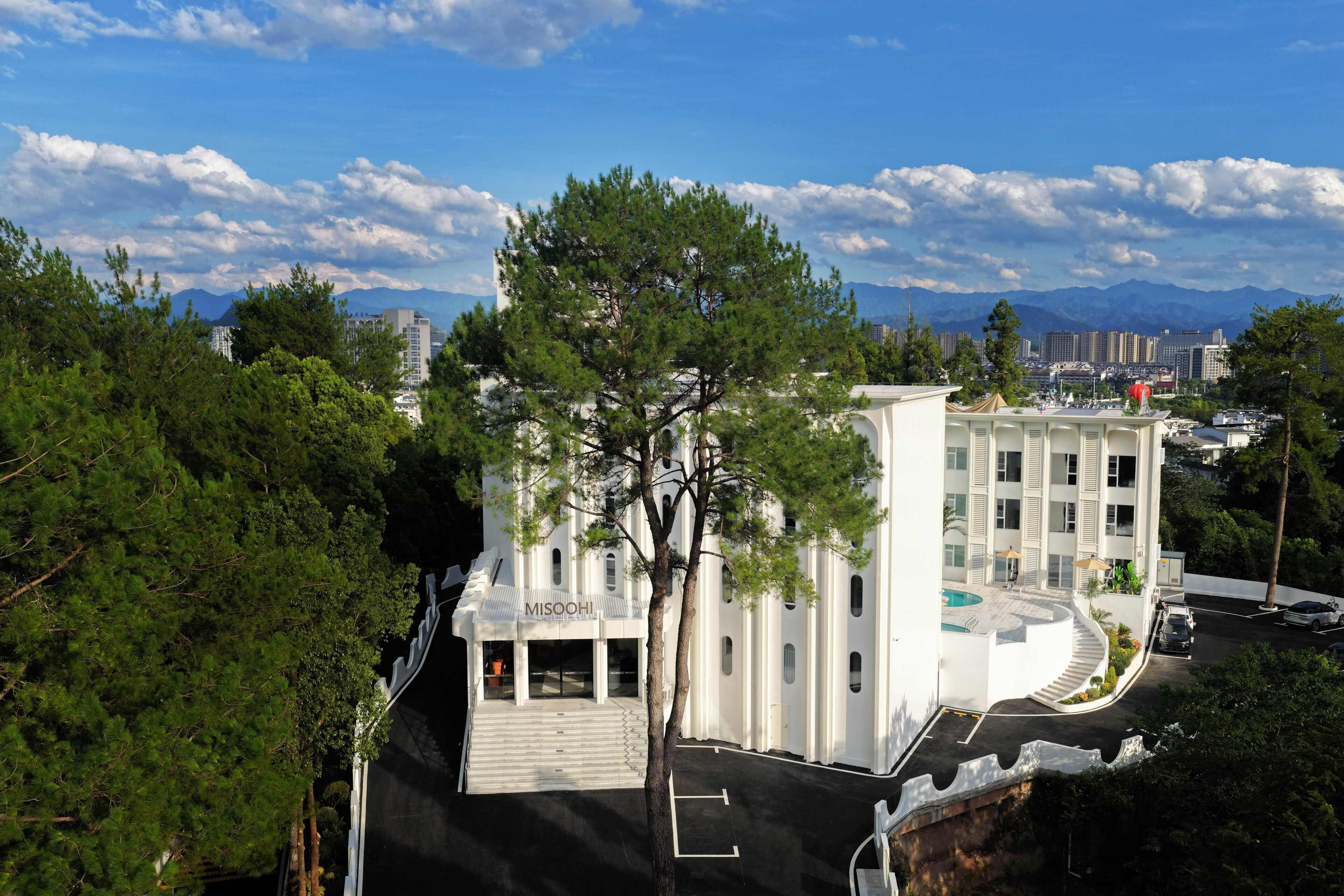 A modern building with a prominent entrance, a swimming pool, and a view of mountains in the background.