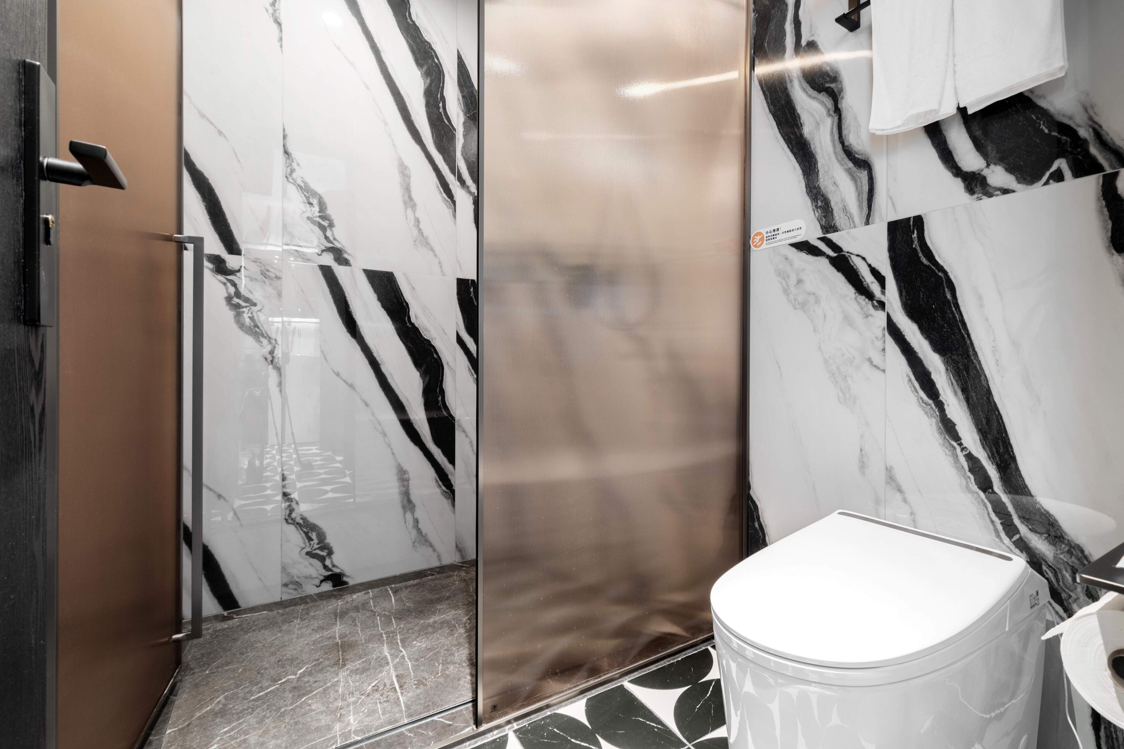 Une salle de bain avec des murs en marbre, des toilettes blanches et un lavabo.