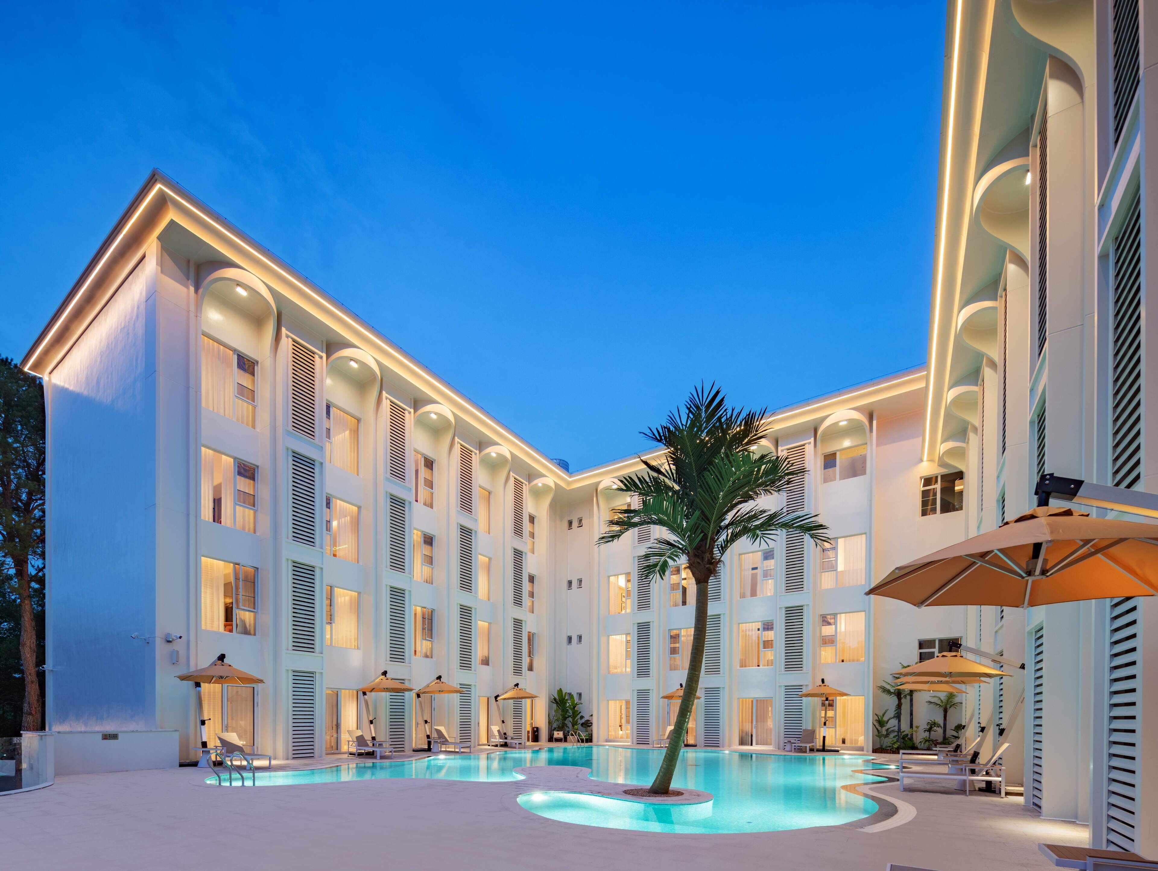 A modern hotel with a central pool, multiple balconies, and outdoor seating areas.