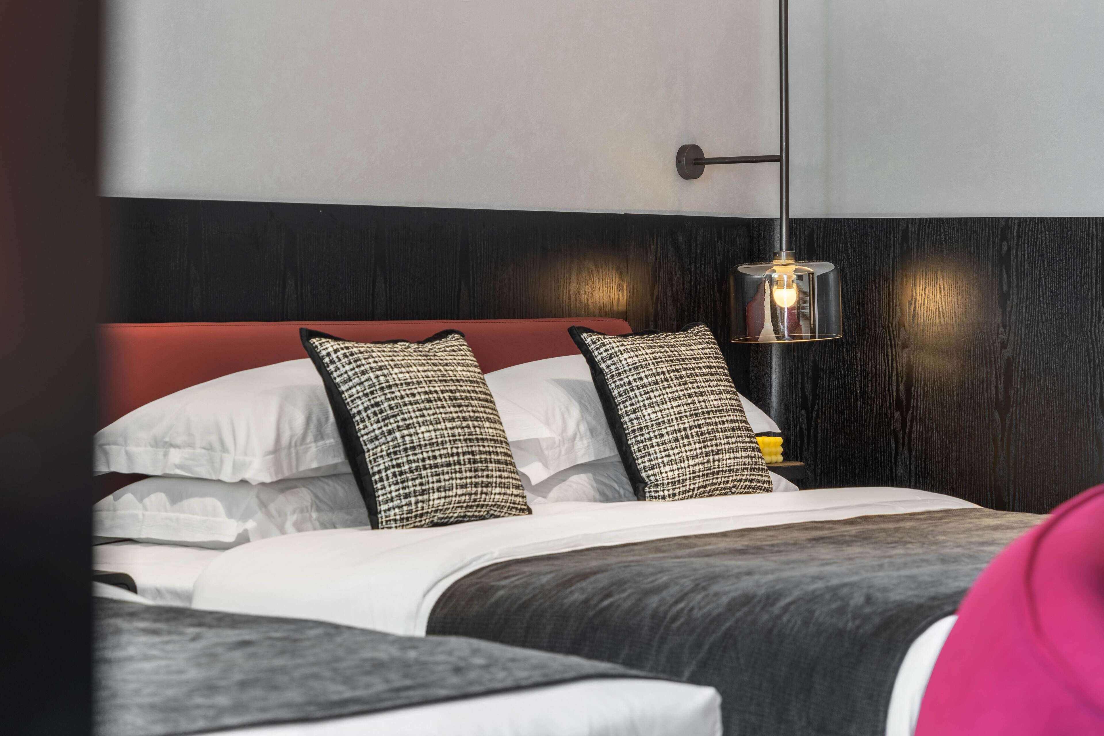 Une chambre d’hôtel avec un lit, des oreillers, une table de chevet et un luminaire suspendu.