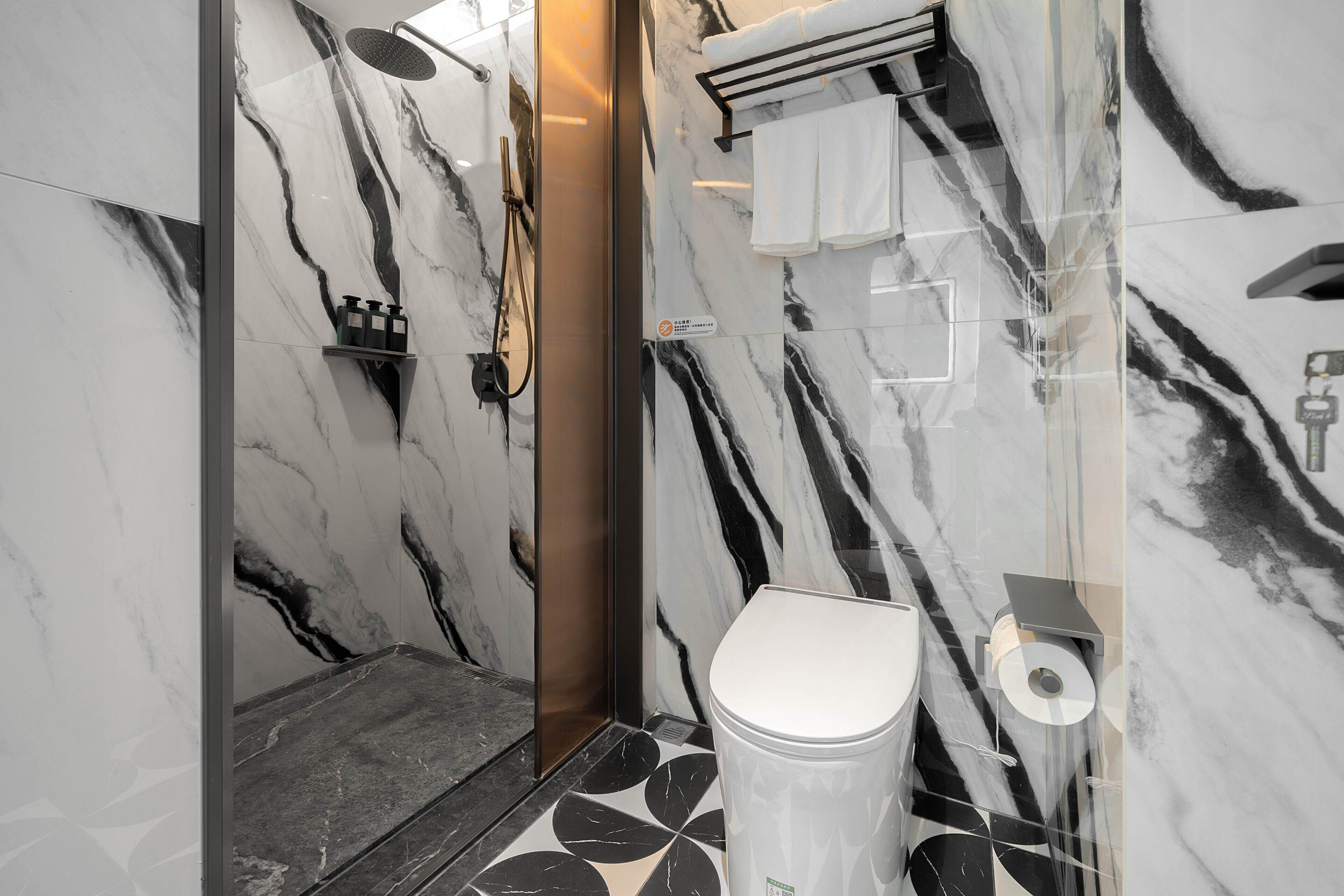 Een moderne badkamer met een marmeren wand, een toilet, een douche en een handdoekhouder.