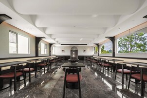 Un comedor amplio con mesas y sillas largas, ventanas grandes y un diseño de techo moderno.