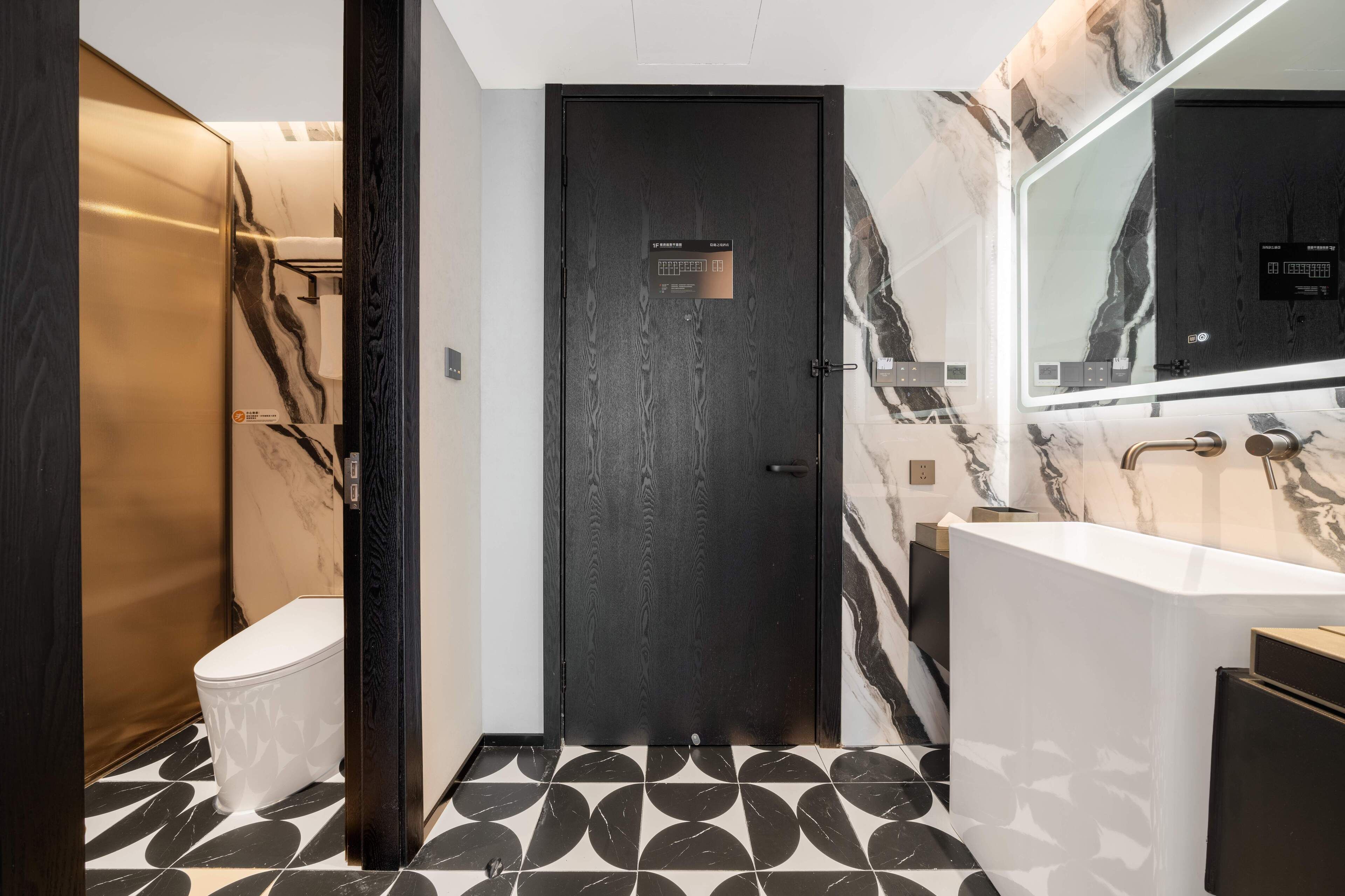 A modern bathroom with a black door, marble walls, and a white sink.