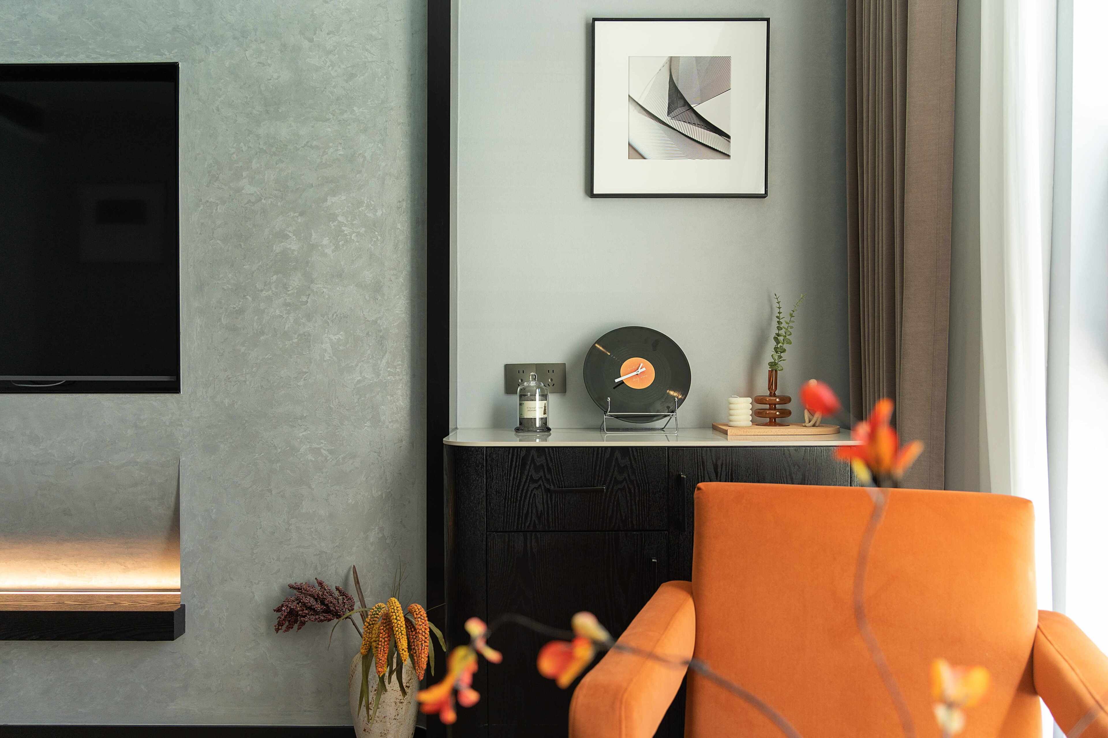 Un salon moderne avec un téléviseur à écran plat fixé au mur, un meuble noir avec un plateau en verre et, au-dessus, une œuvre d’art abstraite encadrée.