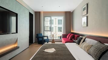 A modern hotel room with a large bed, a flat-screen TV, a red sofa, and a window with a city view.