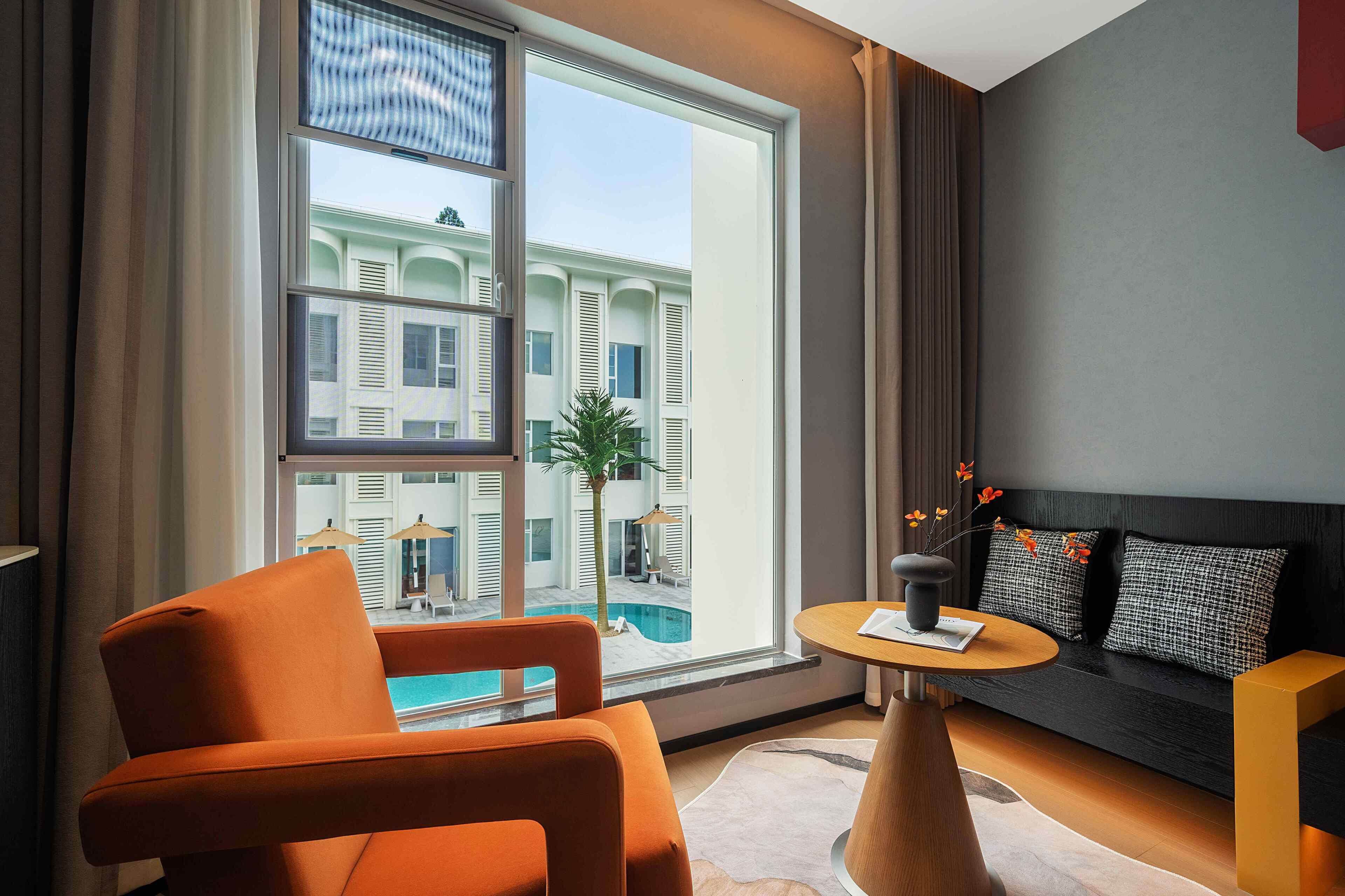 Ein modernes Wohnzimmer mit großem Fenster, einer Couch, einem orangefarbenen Sessel und einem kleinen runden Tisch.