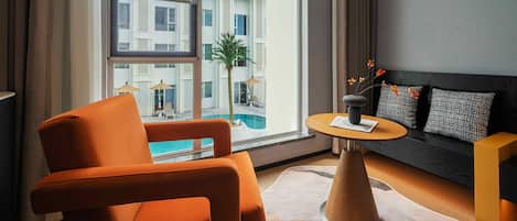 Ein modernes Wohnzimmer mit großem Fenster, einer Couch, einem orangefarbenen Sessel und einem kleinen runden Tisch.