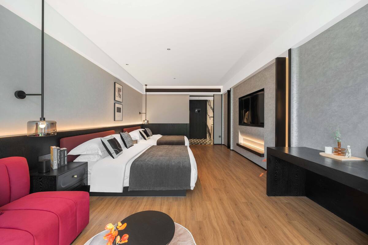 A modern hotel room with a large bed, a red sofa, a TV, and a desk.