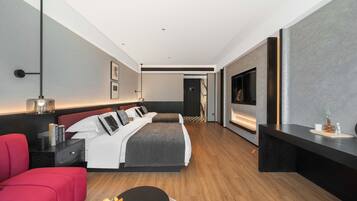 A modern hotel room with a large bed, a red sofa, a TV, and a fireplace.