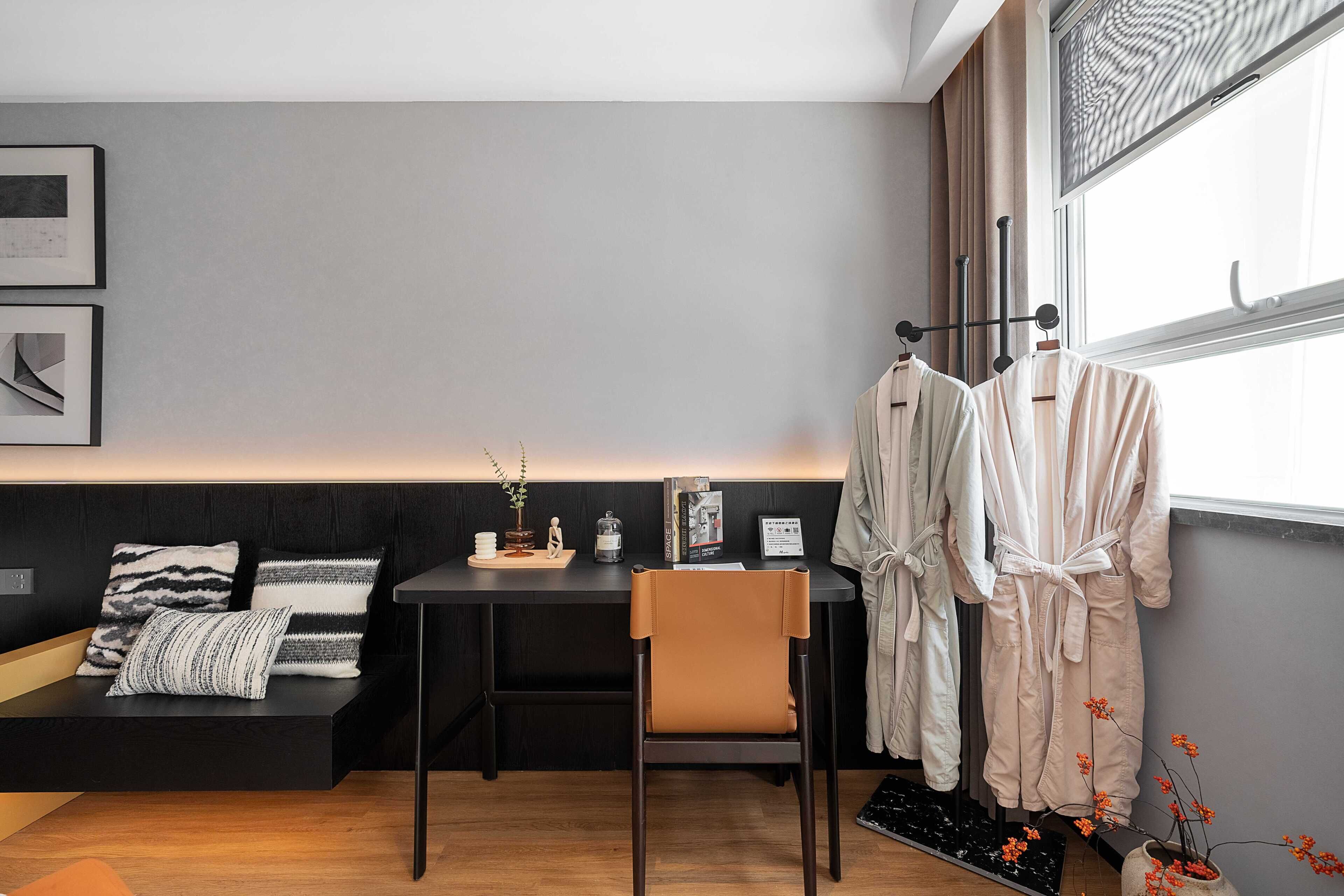 Una habitación moderna con un escritorio negro, un banco acolchado y una ventana con cortinas.