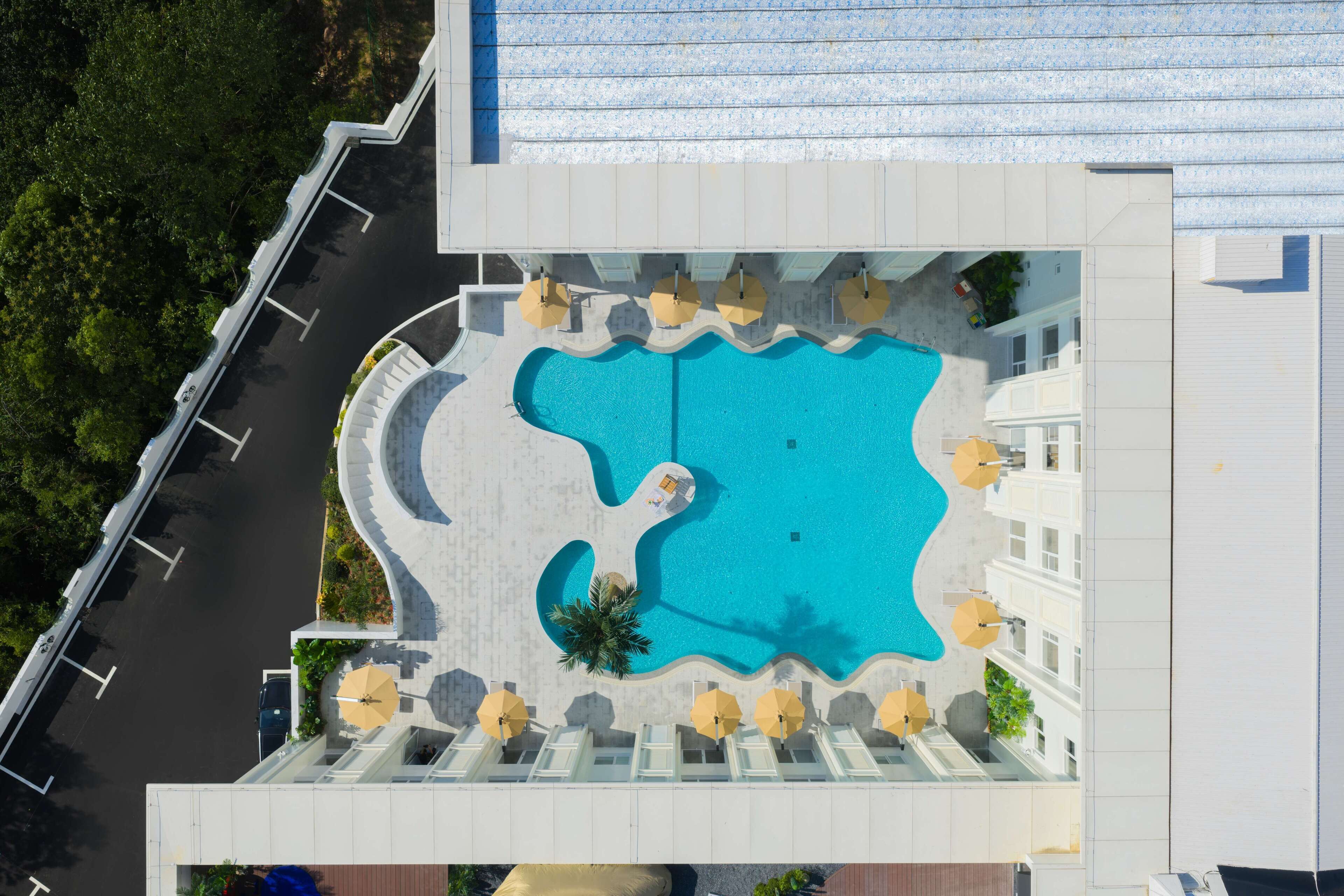 Ilmakuva hotellista, jossa on ainutlaatuinen kitaran muotoinen uima-allas, ja sen ympärillä on aurinkotuoleja ja -varjoja.