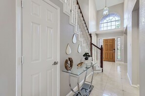 A spacious hallway with a glass railing, white doors, and a wooden staircase.