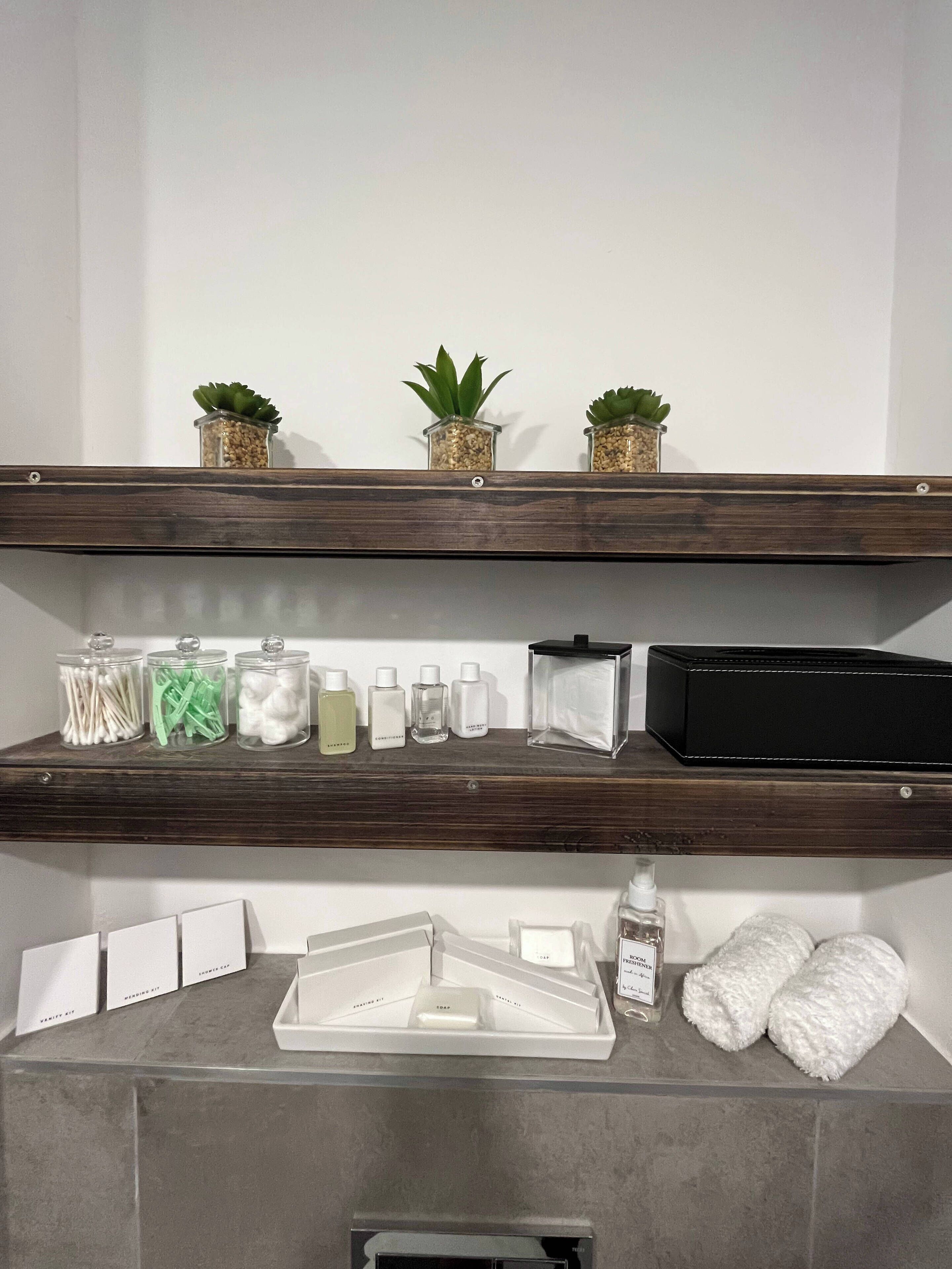 Een badkamer met een houten plank waarop toiletartikelen, een zwarte doos en drie kleine planten in potjes staan.