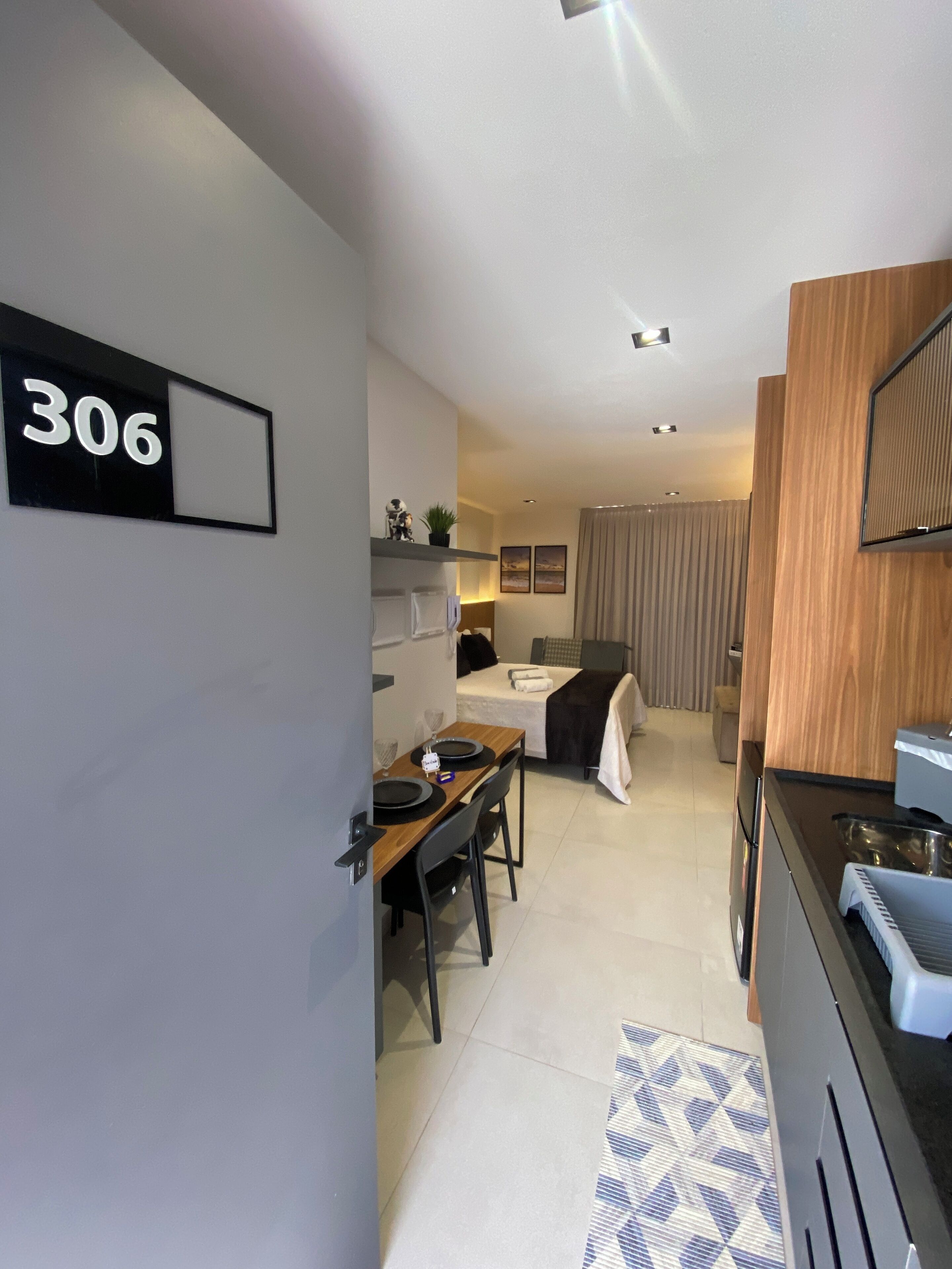 A modern, compact hotel room with a dining area, kitchenette, and a bed.