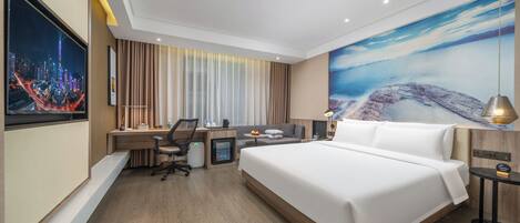Una habitación de hotel moderna con una cama grande, un escritorio con computadora, una silla y una mesita de noche con lámpara.