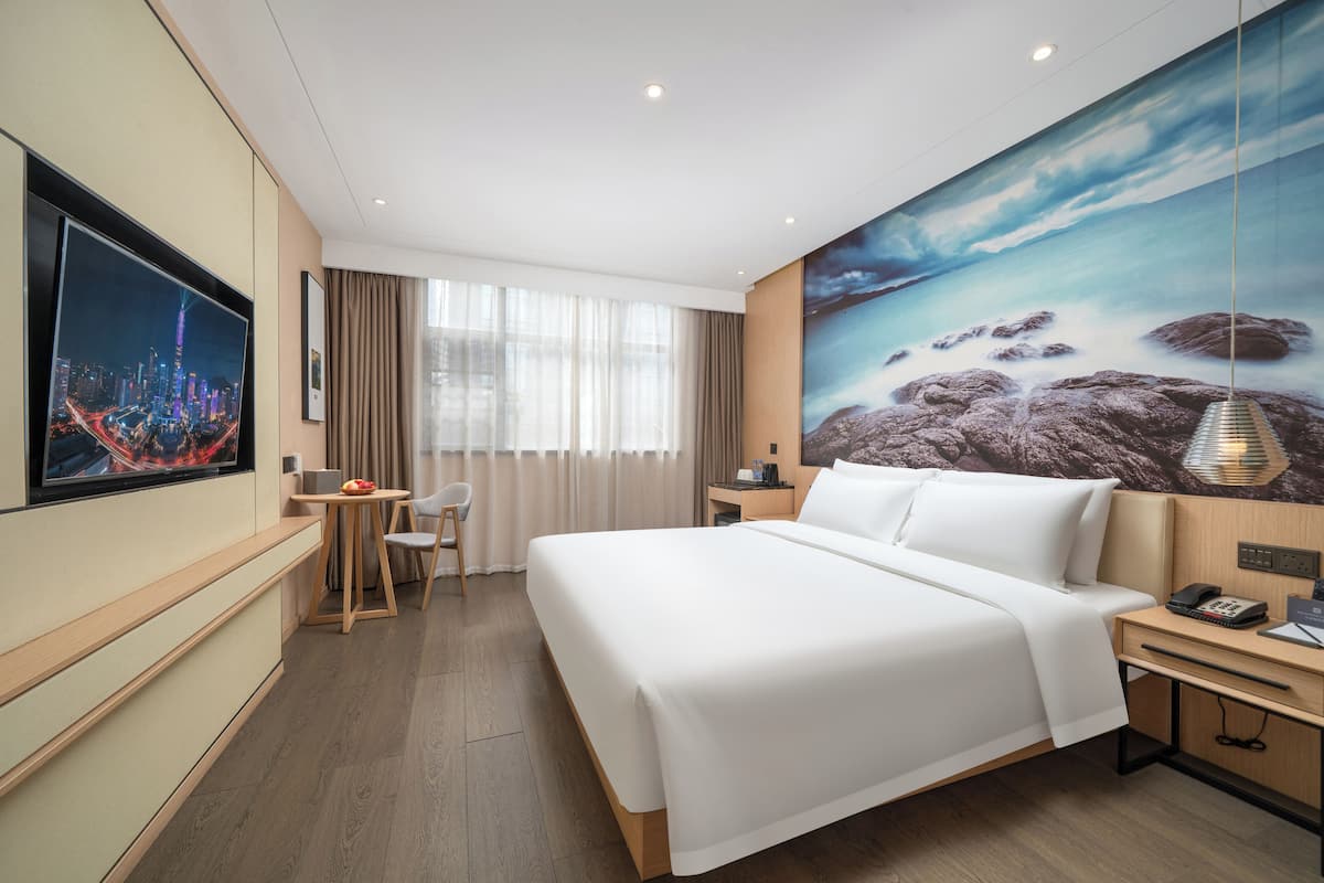 A hotel room with a large bed, a desk, a chair, a TV, and a painting of a landscape.