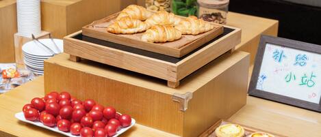 A display of food items including croissants, cherry tomatoes, and custard tarts on a wooden counter.