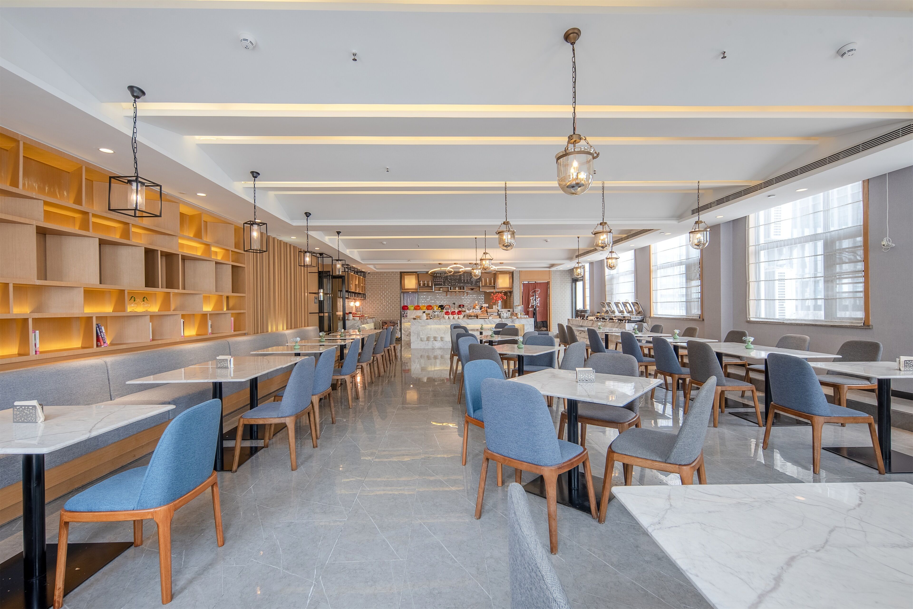 Un ristorante moderno con lunghi tavoli comuni, sedie blu, scaffali in legno e lampade a sospensione.
