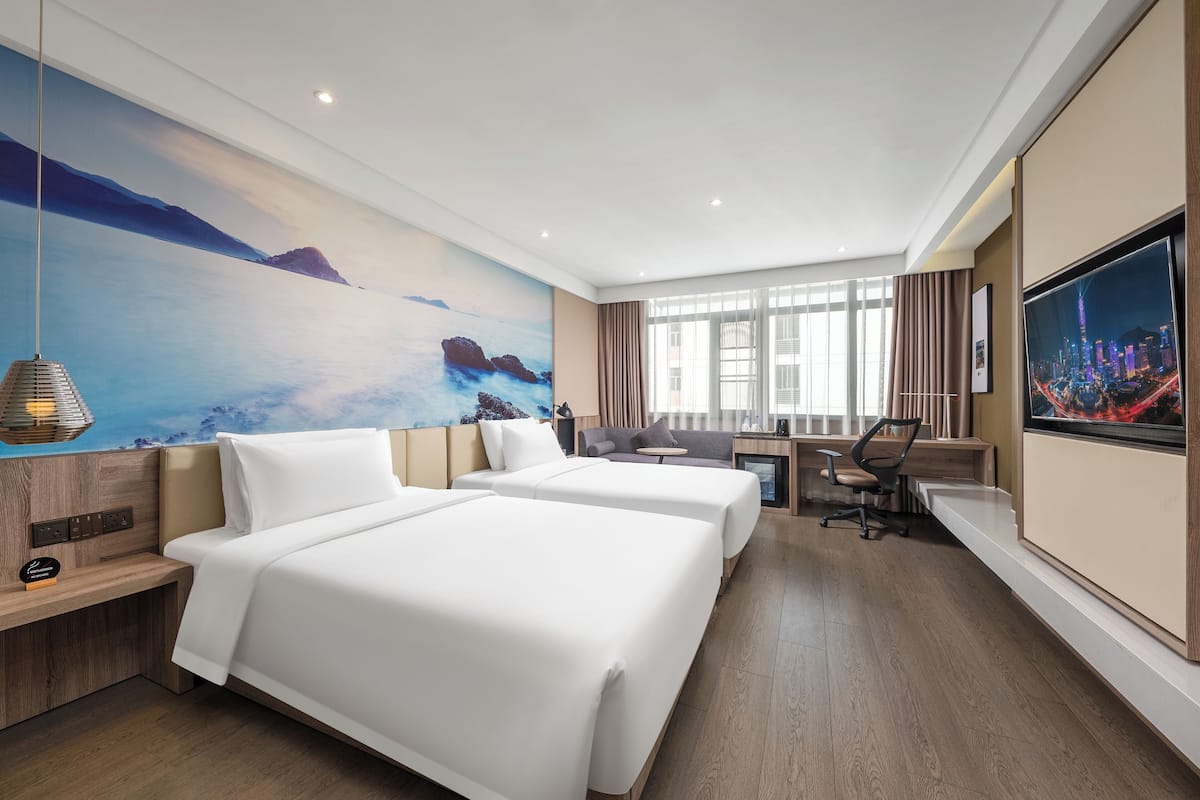 A hotel room with two beds, a desk, a chair, a TV, and a large painting on the wall.