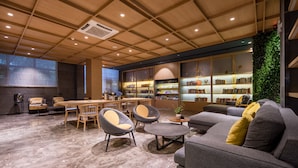 Un interior moderno con techo de madera, una zona de estar central con sillas y sofá, y una estantería llena de libros.