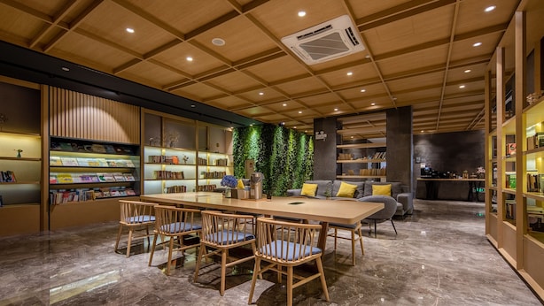 Una biblioteca moderna con techo de madera, estanterías, una mesa central con sillas y una pared verde.