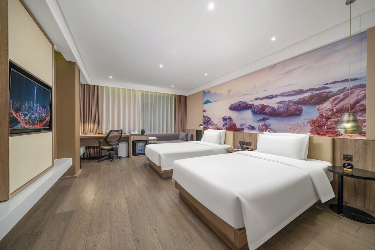 A hotel room with two beds, a desk, a chair, a small table, and a large mural on the wall.
