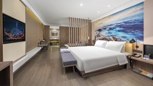 Habitación de hotel moderna con una cama grande, un escritorio, un televisor y un cuadro de una vista marina.