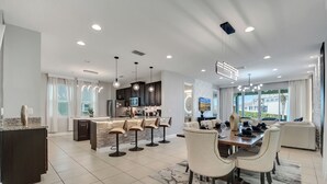 Una cocina moderna con armarios oscuros, una isla central con taburetes de bar y un comedor con mesa de madera y sillas blancas.