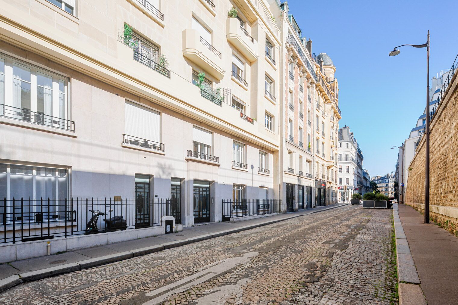 Une rangée d’immeubles à plusieurs étages dotés de balcons, une rue pavée et un trottoir.