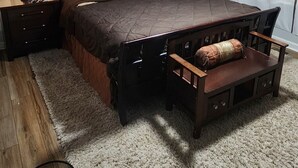 A bedroom with a large bed, a bedside table, a chair, a rug, and a ceiling light.