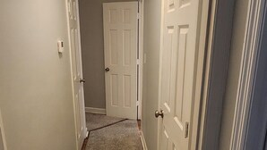 A narrow hallway with carpeted floors, white walls, and a ceiling light fixture.