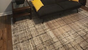 A living room with a dark sofa, two yellow cushions, a glass coffee table, and a black basket.