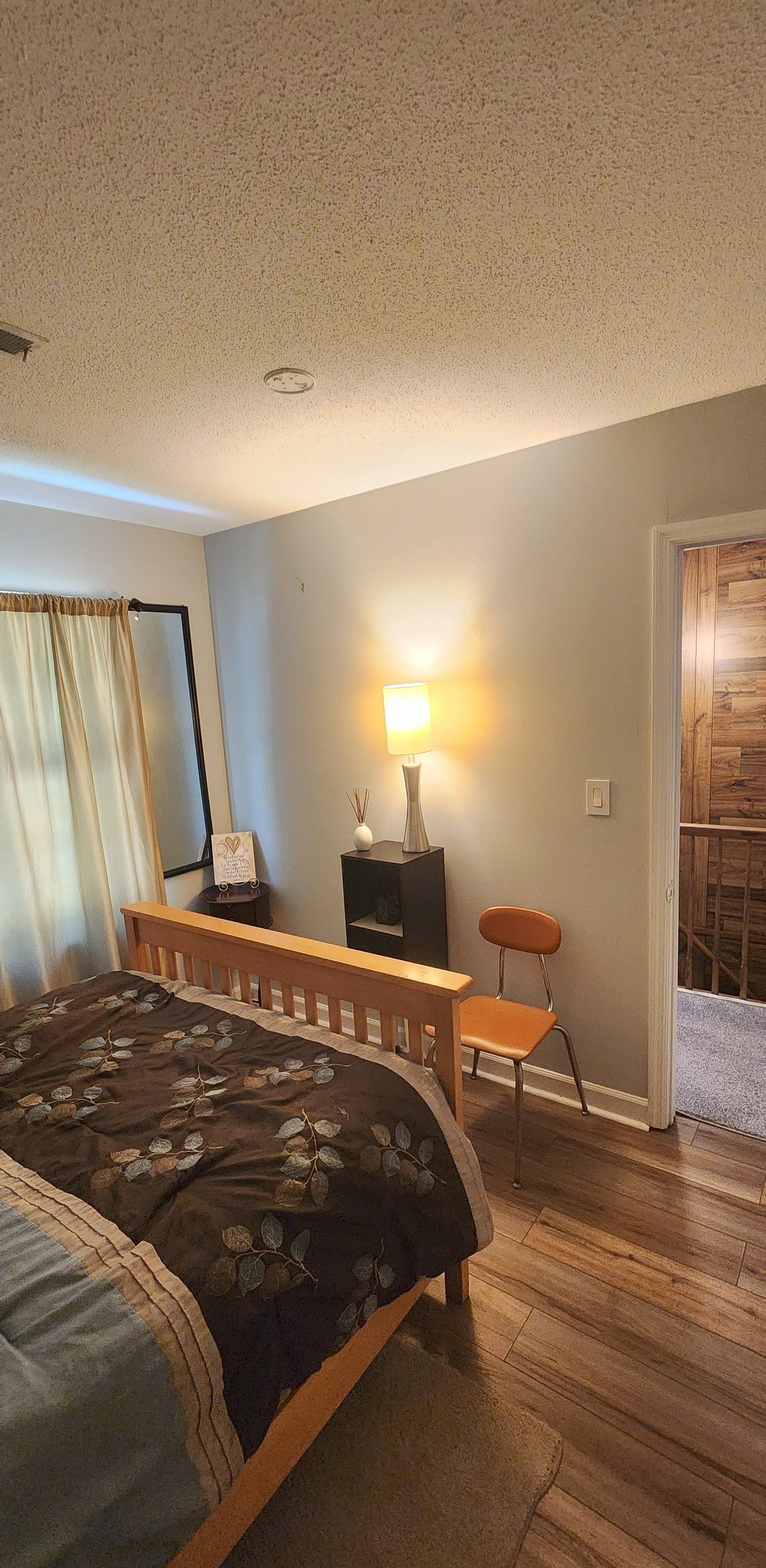 Une chambre à coucher avec un lit, une table de chevet, une lampe, une chaise et une porte en bois.
