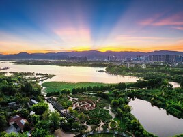 Un parco lungo il fiume con un giardino circolare, un ponte e uno skyline sullo sfondo.