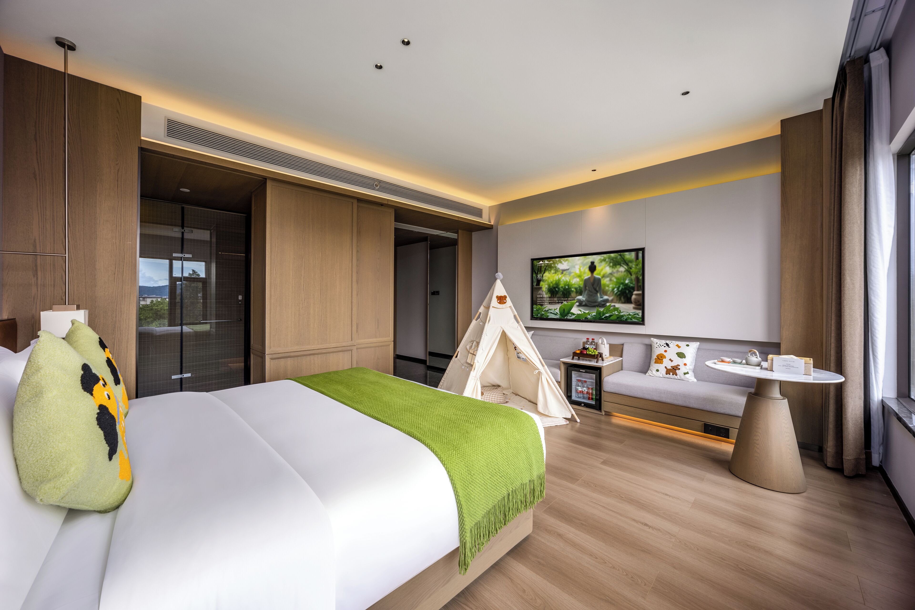 Une chambre d’hôtel moderne dotée d’un grand lit, d’un coin salon aménagé comme une tente, d’un téléviseur à écran plat et d’une petite table.