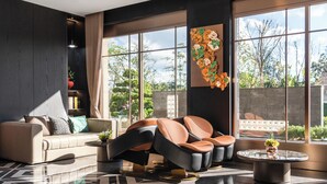 Una sala de estar moderna con un sofá, sillas, una mesa de centro y ventanas amplias que ofrecen vistas al exterior.