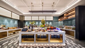 Un lobby moderno de hotel con un mostrador de recepción de mármol, una zona de bufé con diversas opciones de comida y un piso de baldosas.