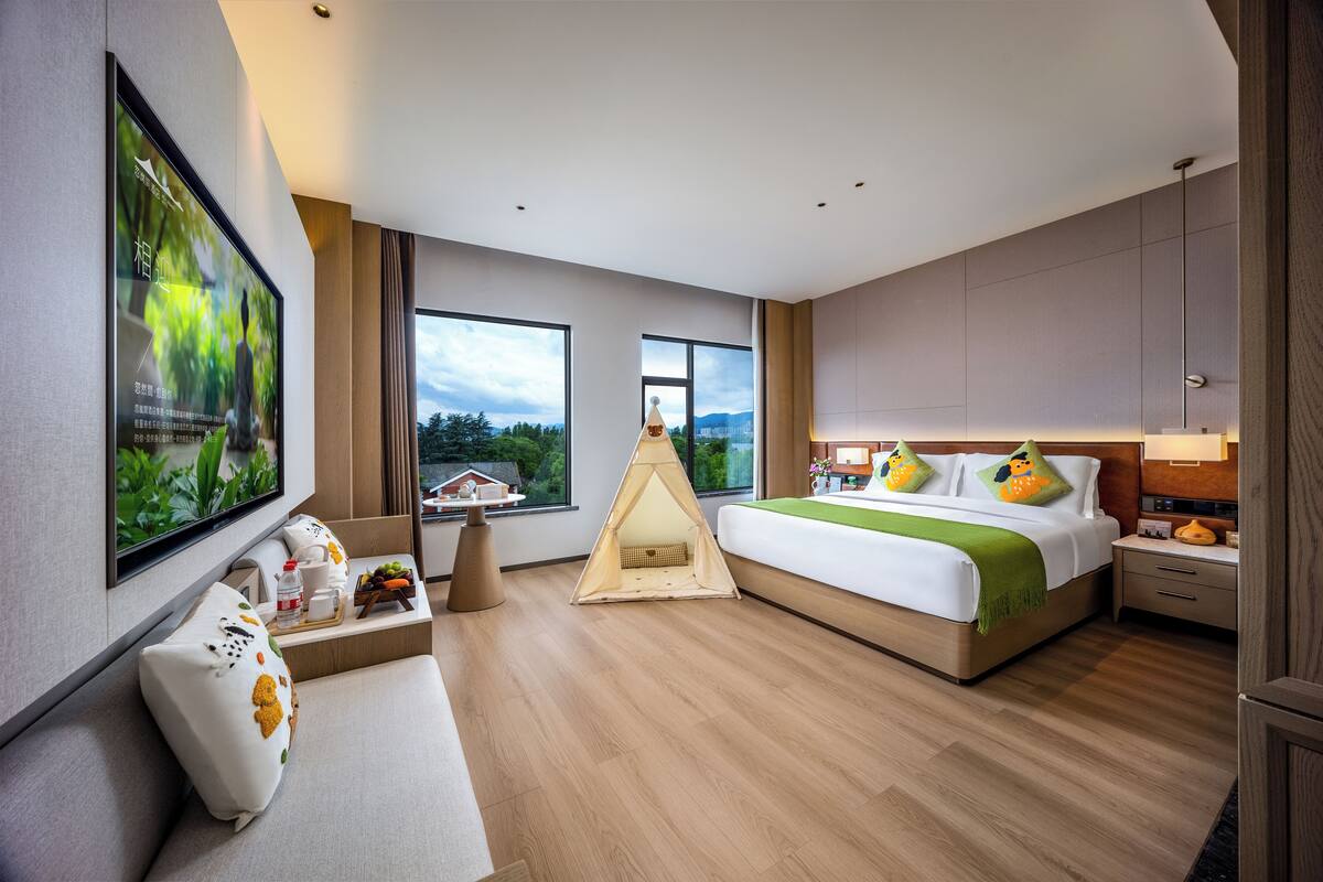 A modern hotel room with a large bed, a seating area, a tent, and a television on the wall.