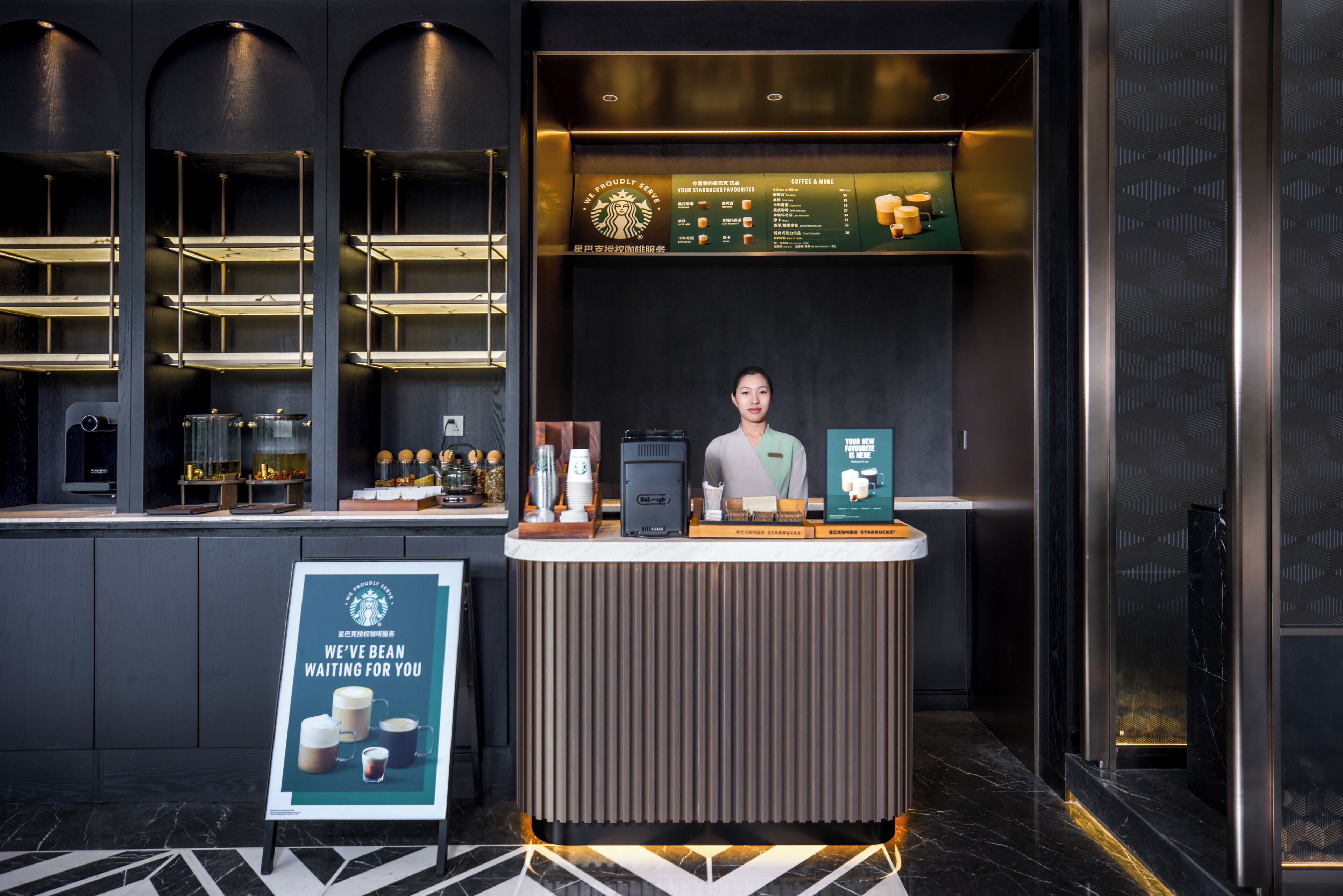 L’intérieur d’un café Starbucks, doté d’un design moderne, comprenant un comptoir avec un tableau affichant le menu, une machine à café et un panneau indicateur.