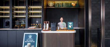Interior de una cafetería Starbucks con un diseño moderno, que incluye un mostrador con un tablero de menú, una máquina de café y un cartel.