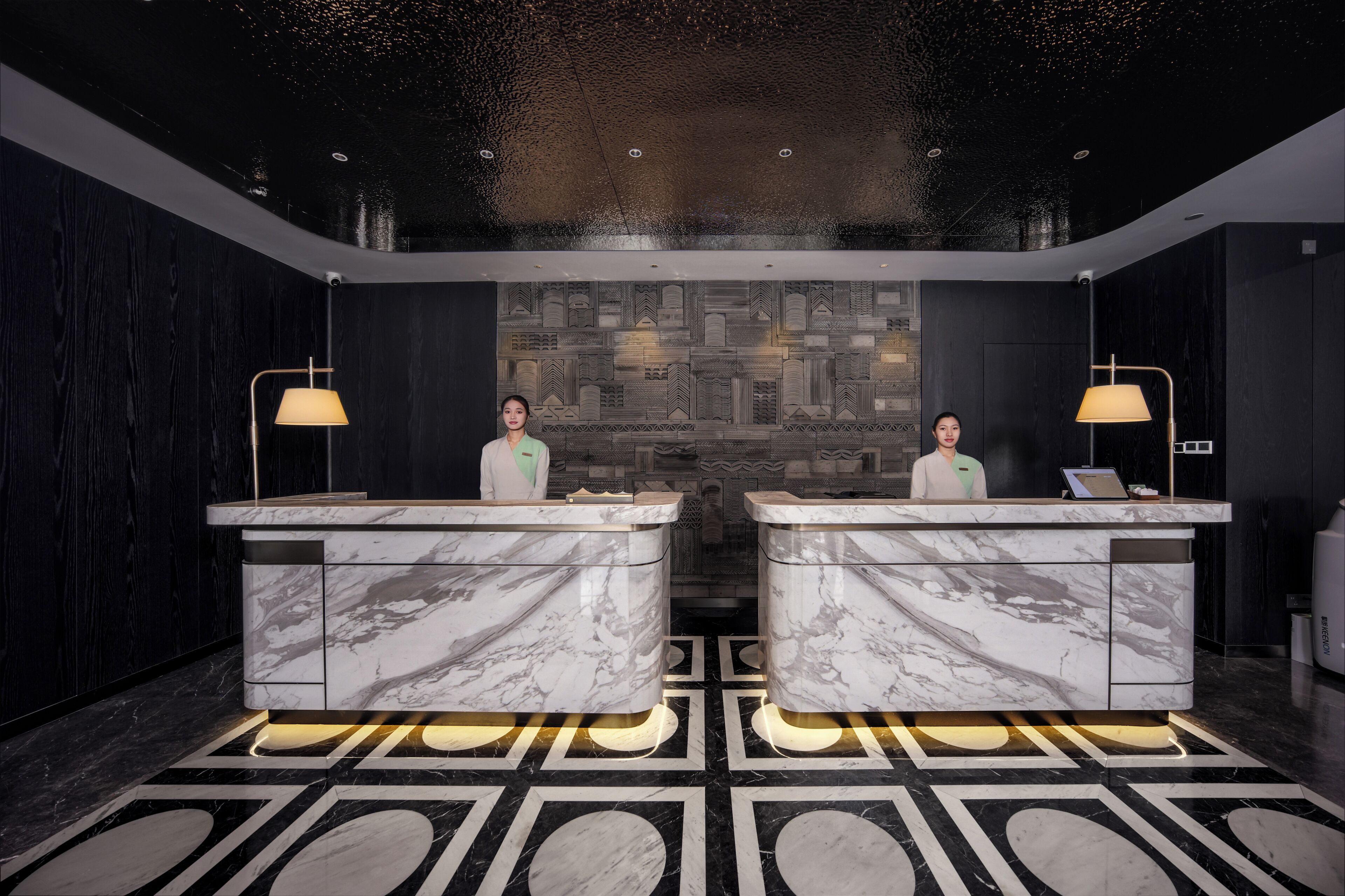 A reception area with marble counters, two receptionists, and a patterned wall in the background.