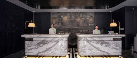 A reception area with marble counters, two receptionists, and a patterned wall in the background.