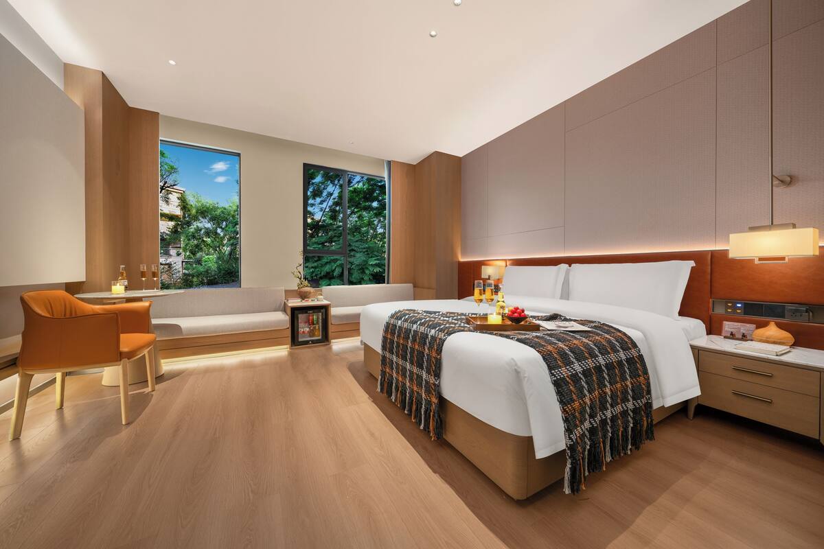 A modern hotel room with a large bed, bedside tables, a desk, and a view of the outdoors.