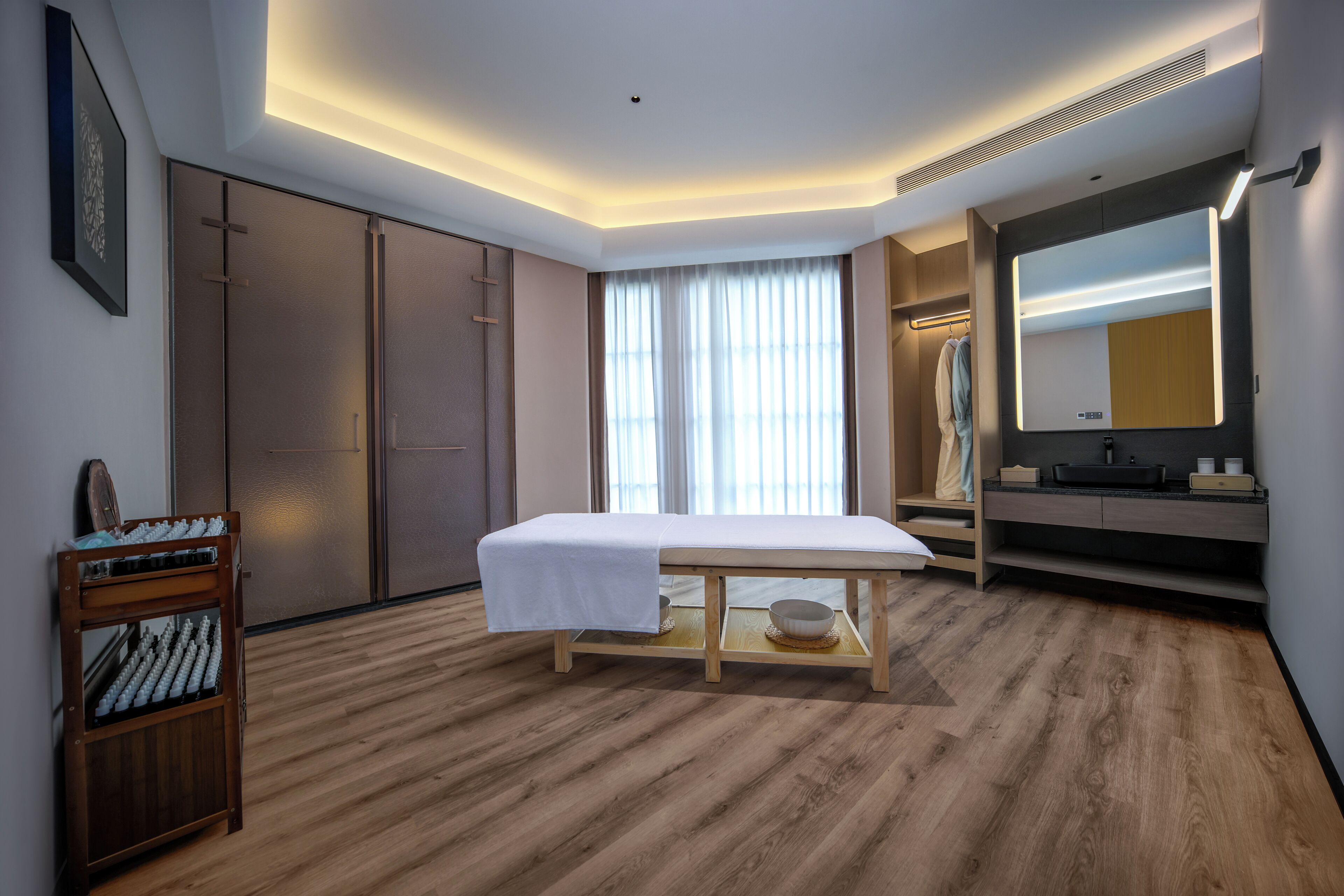 Una habitación de hotel moderna con suelo de madera, una mesita de noche con una toalla blanca, un espejo grande y un armario.