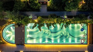 Una piscina en la azotea con diseño de olas, rodeada de vegetación y zonas de descanso.