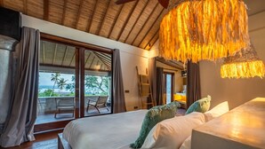 A bedroom with a large bed, a balcony with a view, and a hanging light fixture. - Infinity Pool | Five Bedrooms | Beachfront Stay (Canggu)